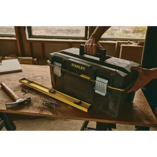 STANLEY 023001W toolbox on workbench with hammer, nails, and level, person holding handle, workshop background.