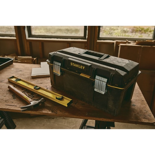 Stanley 023001W toolbox with metal latches on a workbench, hammer and level nearby, workshop setting.