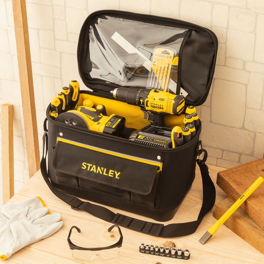 STANLEY 1-96-193 tool bag filled with yellow and black hand tools, drill, accessories, on wooden table.
