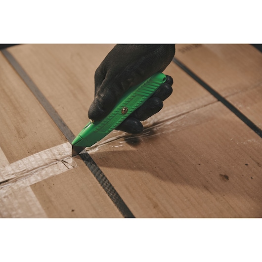 Photo of STANLEY 10-179 utility knife cutting tape on a cardboard box, gloved hand holding green knife.