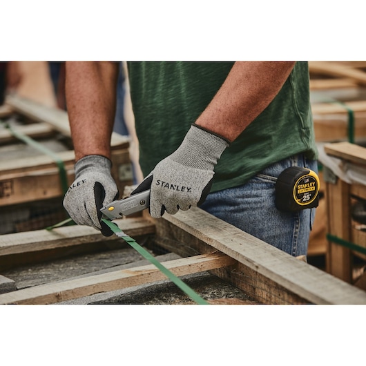 Stanley 10-499 utility knife in use, worker with gloves cutting green strapping on wooden pallet.