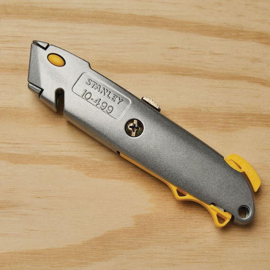 STANLEY 10-499 utility knife, gray metal body with yellow accents, side angle, on wooden surface.