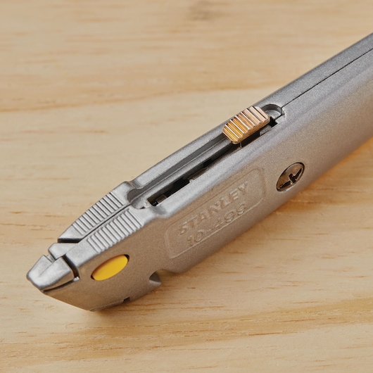 STANLEY 10-499 utility knife in silver, close-up angle on wood surface, showing blade slider and yellow button.