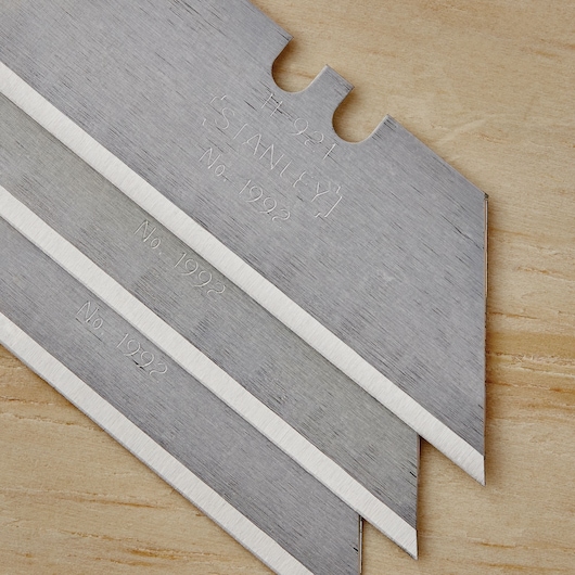 STANLEY 10-499 utility knife blades, silver color, close-up, stacked on wood surface, sharp edges visible.