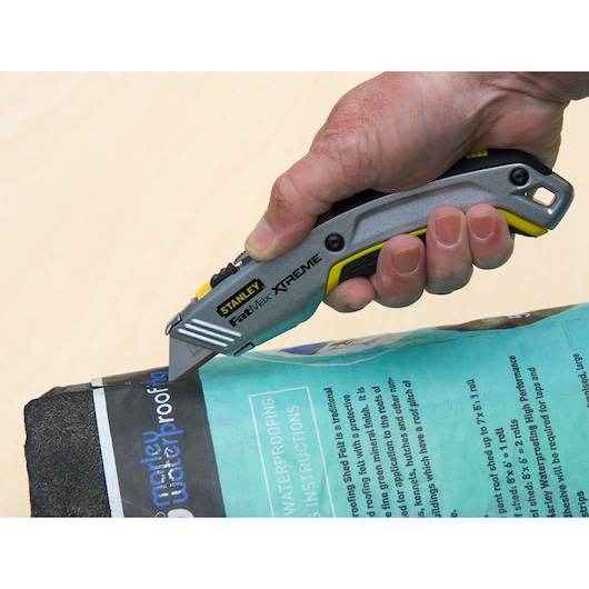 Photo of STANLEY 10-789 utility knife cutting waterproofing material, close-up view of tool in hand.