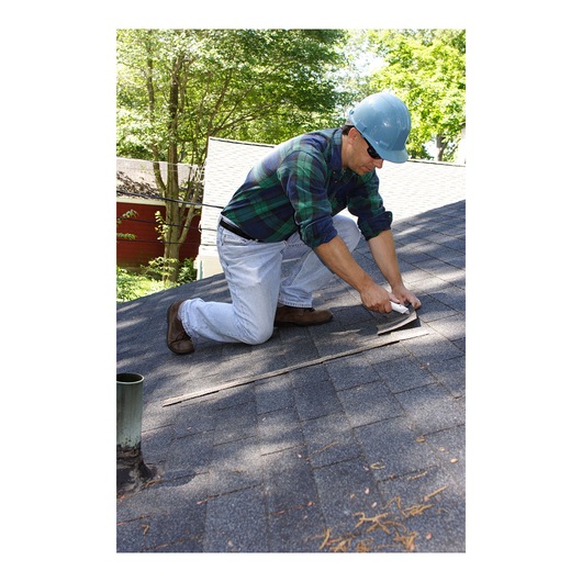 Photo of STANLEY 10-789 utility knife in use for rooftop shingle repair, person kneeling on gray roof.