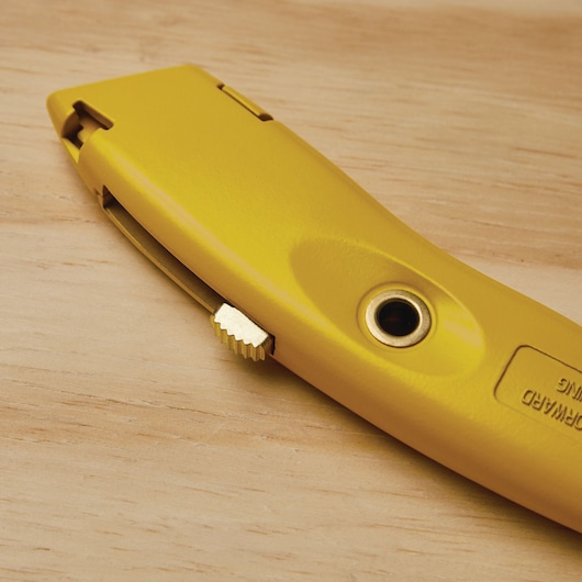 STANLEY 10-989 utility knife side view on wood surface, yellow metal body with thumb wheel and blade slot visible.