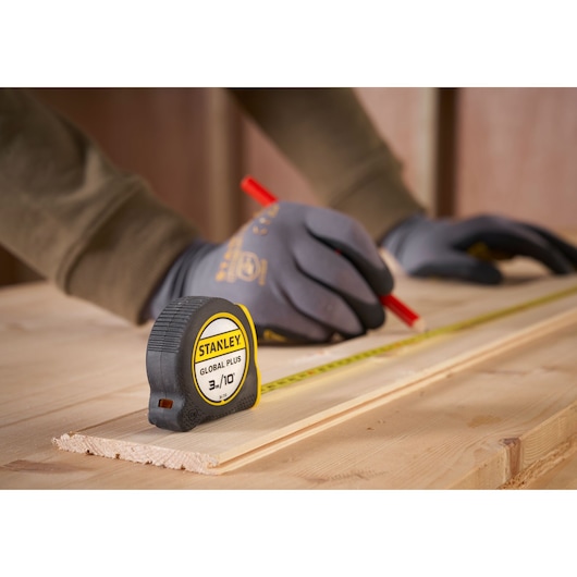 STANLEY 30-710 tape measure on wood, person with gloves marking a board with pencil.