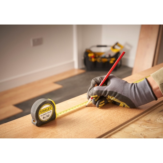 Photo of STANLEY 30-710 tape measure on wood plank, worker marking measurement, tool bag in background.