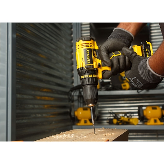 Stanley SCD20C2K cordless drill in use drilling into wood, close-up, yellow and black tool.