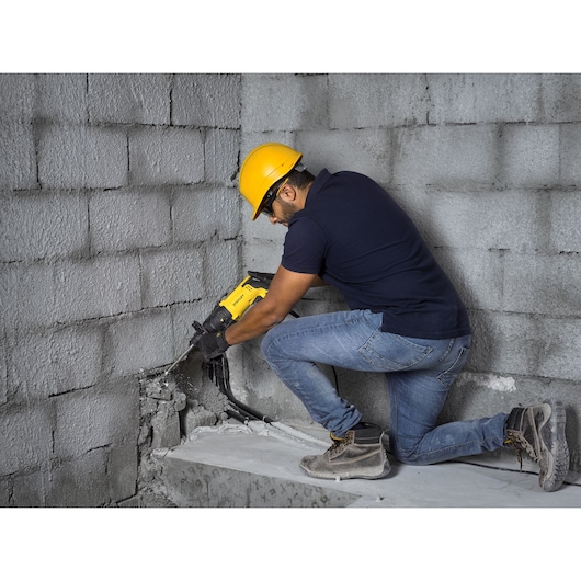 Photo of STANLEY SHR263K-BR rotary hammer used on concrete wall by worker wearing safety helmet.