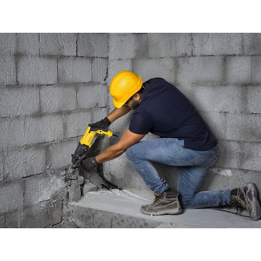 STANLEY SHR263K-BR rotary hammer drill in use on concrete wall, side angle photography.