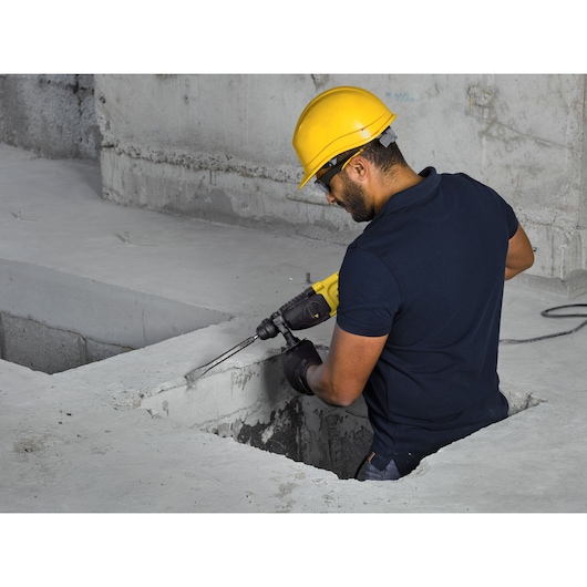 Stanley SHR263K-BR rotary hammer used on concrete, side angle, by worker with yellow helmet.