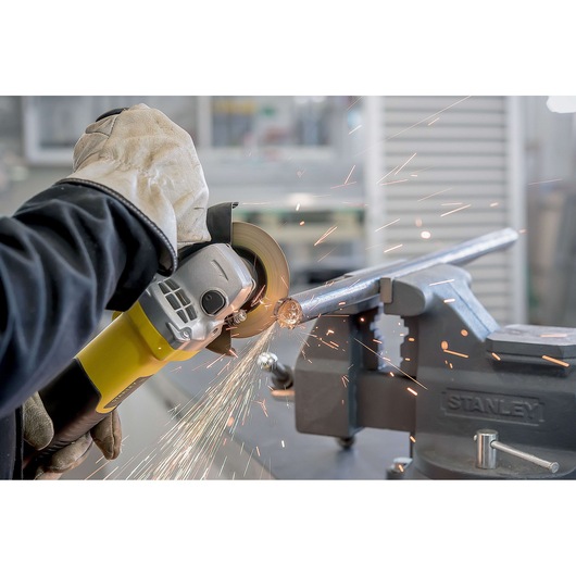 Photo of STANLEY STA8061 grinder in use cutting metal pipe held by vise, visible sparks, close-up action shot.