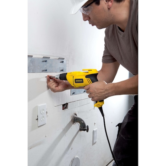 Stanley STDR5206 electric heat gun in use for wall repair, close side view, yellow and black finish.
