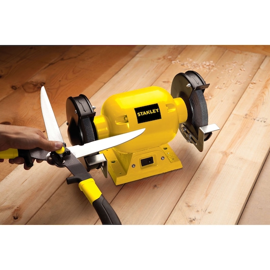 STANLEY STGB3715 bench grinder sharpening garden shears, yellow and black tool, on wooden surface, front angle.