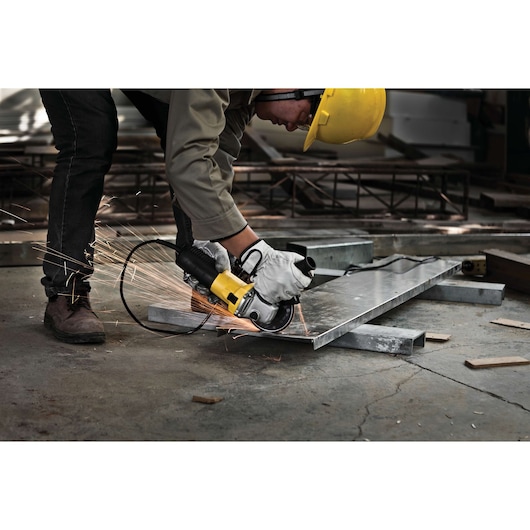 STANLEY STGS6115 angle grinder cutting metal sheet, worker wearing gloves and yellow helmet, workshop setting.
