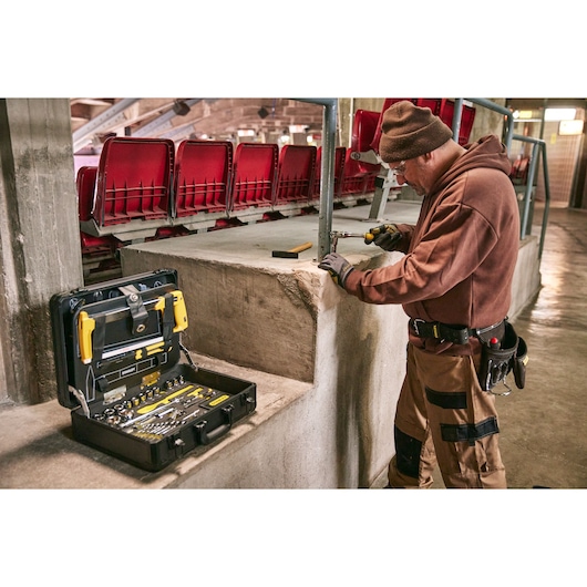 STANLEY STMT98109-LA mechanic tool set with case open on concrete surface, worker using tools in stadium seating area.