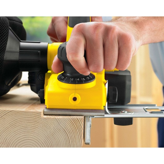Photo of STANLEY STPP7502-B2 electric planer in use on wood, close-up of adjustment knob and front grip.