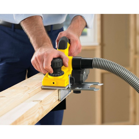 Photo of STANLEY STPP7502-B2 yellow hand planer smoothing wood, hose attached, woodworking setting.