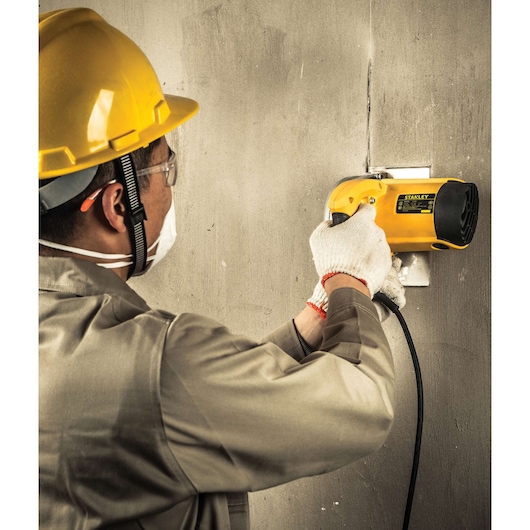 STANLEY STSP125-KR angle grinder in use cutting wall, shown from side, yellow casing, held by worker.