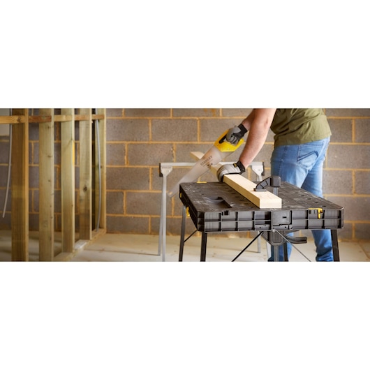 STANLEY STST11552 workbench in use, black folding table holding wood plank in workshop setting.