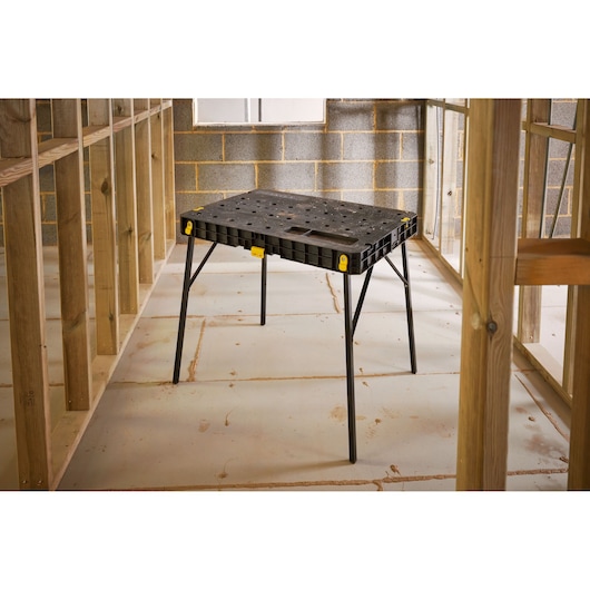 STANLEY STST11552 black plastic folding workbench with metal legs, shown at an angle in construction setting.