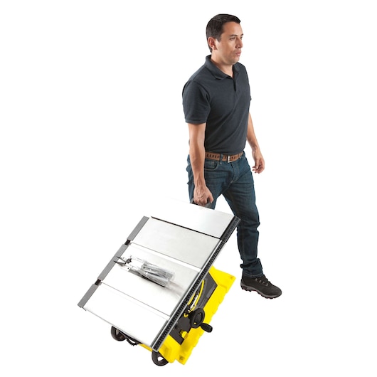 Photo of a man carrying a STANLEY STST1825 portable table saw with yellow base, side angle view.